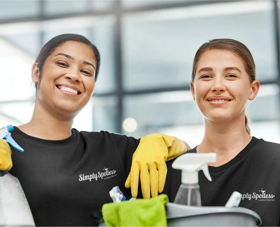 Two Simply Spotless workers smiling and holding cleaning equipment