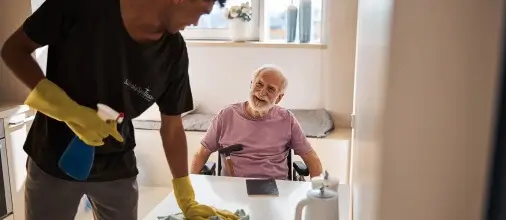 Simply Spotless Cleaner cleaning a kitchen space during an NDIS cleaning service, whilst engaging with the customer and smiling